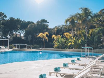 Ein Außenpool mit weißen Liegestühlen und Palmen im Hintergrund unter klarem Himmel.