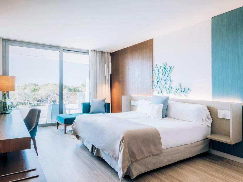 Bright hotel room with large bed, desk, chair, and window with natural light.