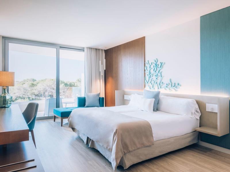 Modern hotel room with large window, double bed, desk, and seating area.