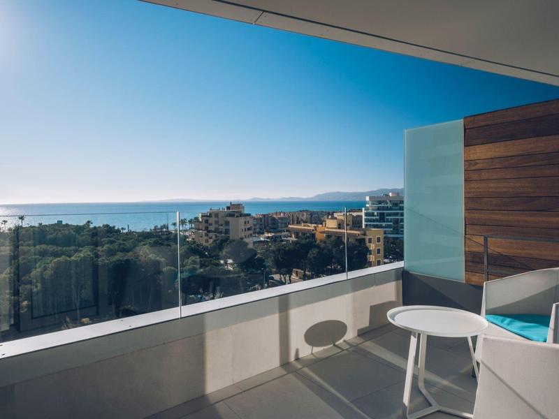 Modern balcony with glass railing overlooking the sea and buildings under clear sky.