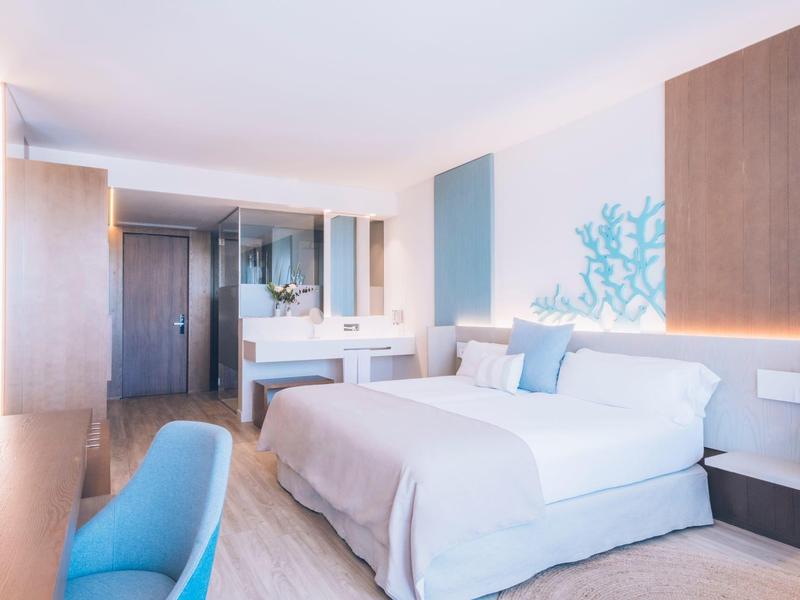 Bright hotel room with a large bed, blue chair, wooden accents, and modern decor.
