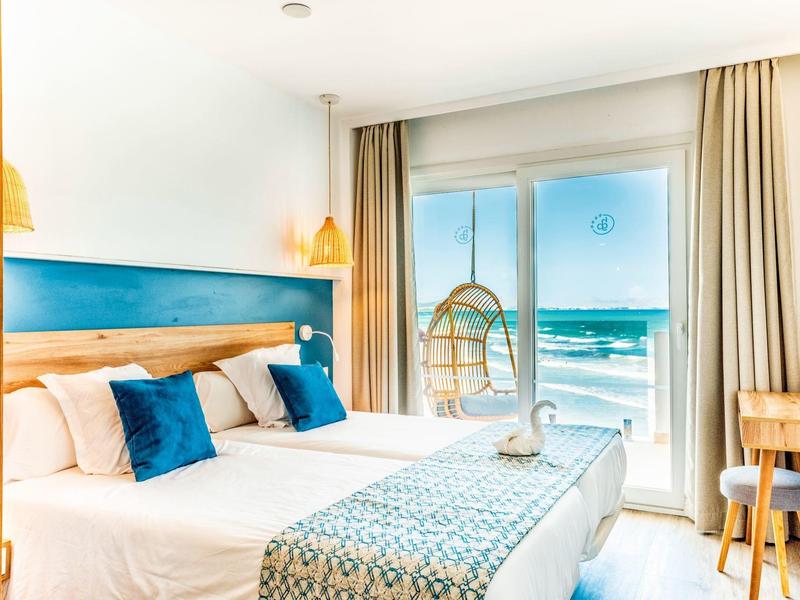Brightly furnished hotel room with balcony and sea view.