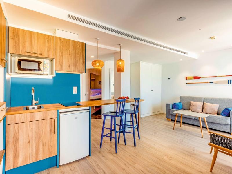 Modern living area with kitchenette, blue accents, and cozy sofa in hotel room.