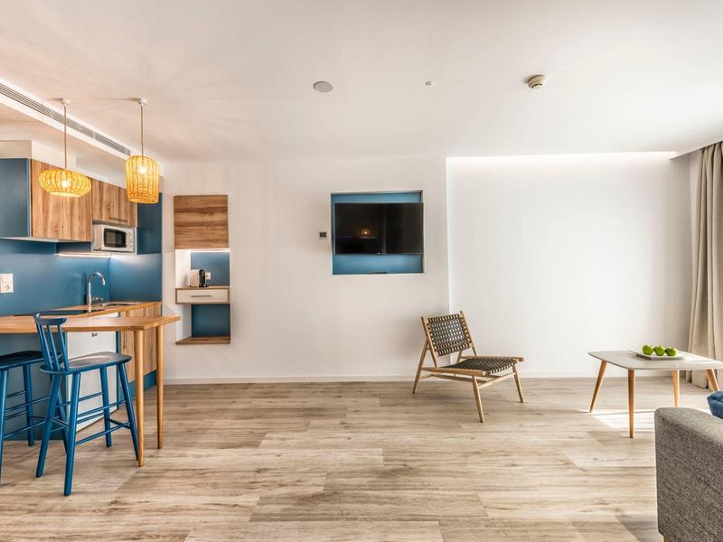 Modern living area with wood flooring, open kitchen, and seating in a hotel room.