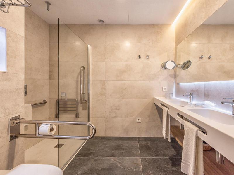 Accessible bathroom with shower, grab bars, and long lit mirror.