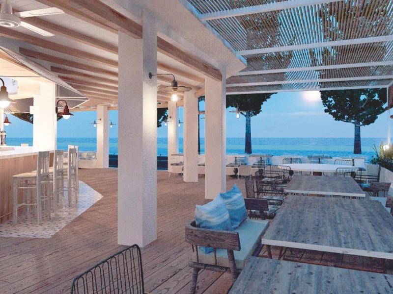 Terrasse extérieure d'un hôtel avec vue sur la mer, tables en bois et sièges confortables.