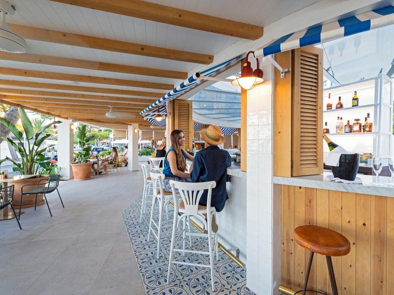 Bar en plein air avec chaises hautes, toiture en bois et décor tropical dans un hôtel.