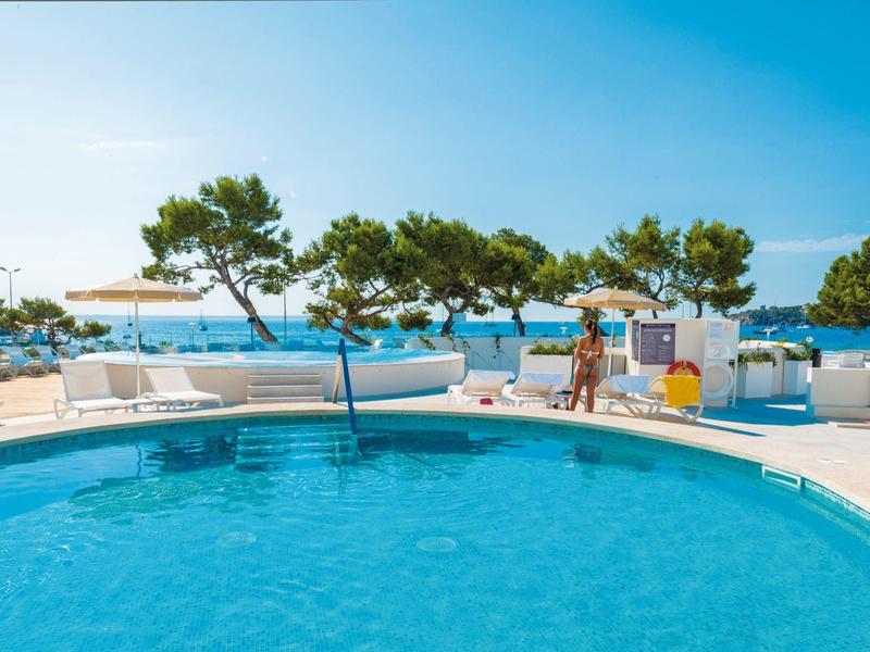 Piscine ronde bleu avec vue sur la mer et chaises longues blanches sous un ciel clair.
