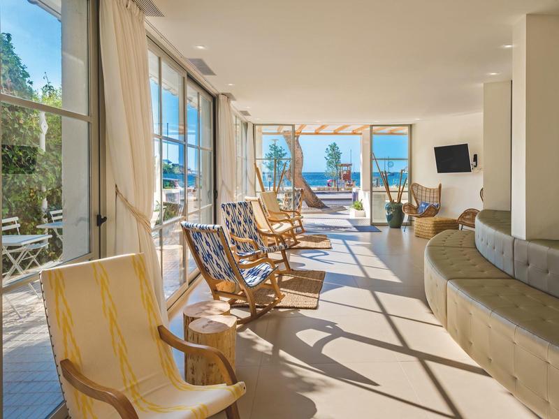 Salon lumineux avec fauteuils et grande baie vitrée donnant sur une terrasse et vue sur mer.