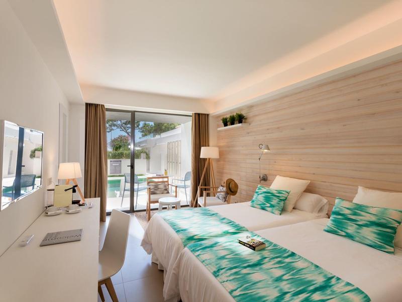 Chambre d'hôtel moderne avec deux lits, décor tropical et terrasse ensoleillée.