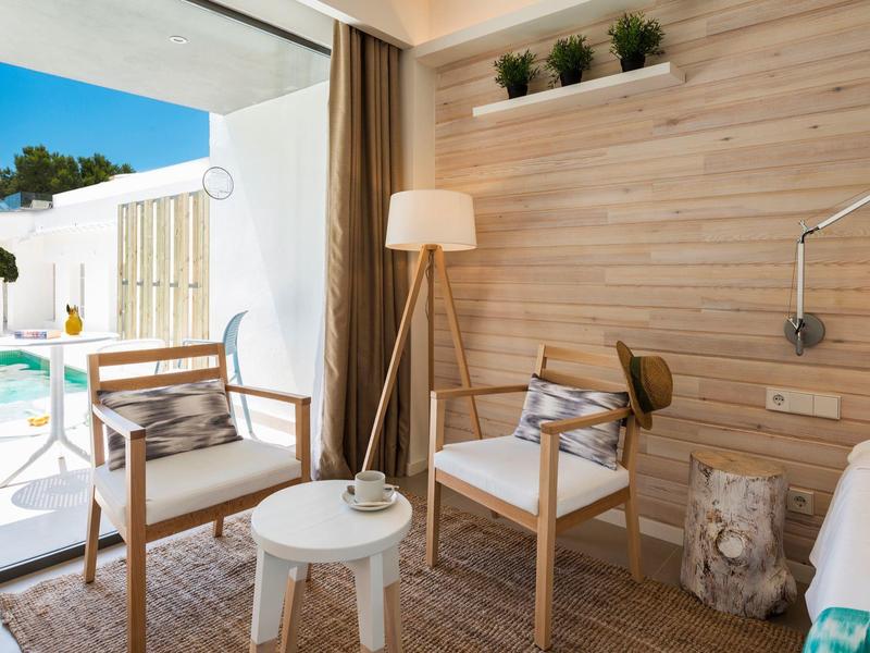 Coin salon lumineux avec deux fauteuils, table blanche et vue sur piscine en extérieur.