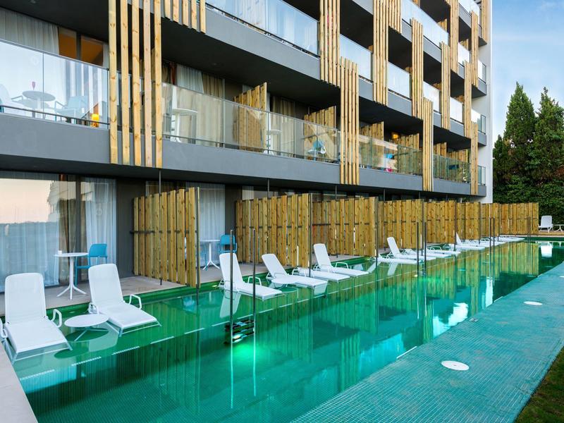 Piscine moderne avec chaises longues blanches devant immeuble d'appartements.