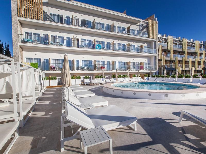 Piscine circulaire avec chaises longues devant un hôtel moderne sur fond de ciel bleu.