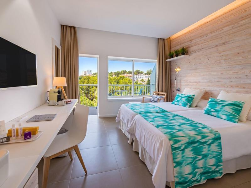 Chambre d'hôtel moderne avec lit double, bureau, TV et balcon donnant sur un paysage.