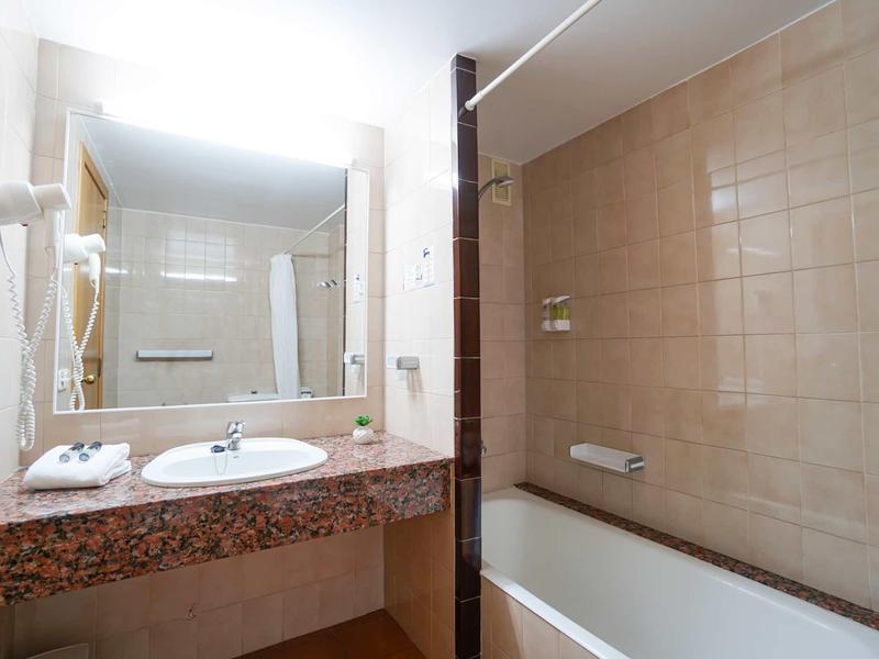 Bagno dell'hotel con lavabo e vasca da bagno, piastrelle beige e grande specchio