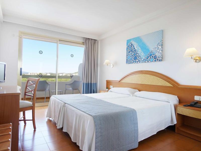 Camera d'hotel luminosa con letto matrimoniale, scrivania, sedia e balcone con vista.