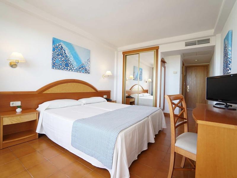 Camera d'hotel semplicemente arredata con letto matrimoniale, scrivania, sedia e TV.