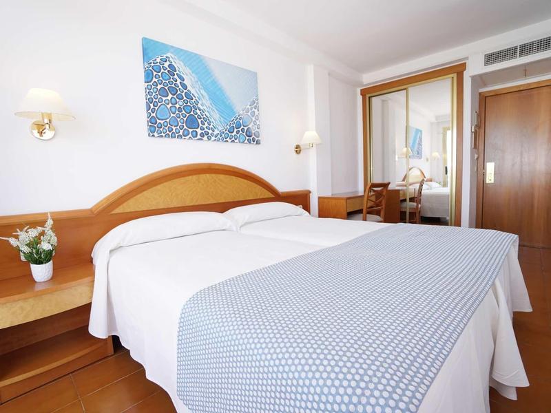 Camera d'hotel luminosa con letto matrimoniale, comodini e area scrivania.