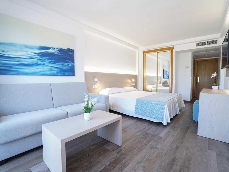 Camera d'hotel moderna con letto matrimoniale, divano, tavolo e quadro del mare sulla parete.