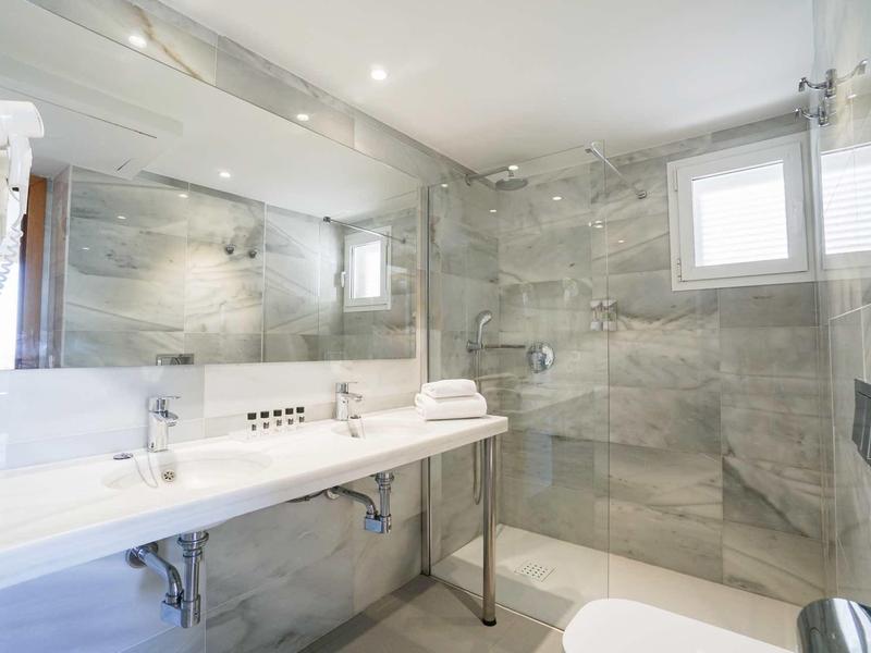 Bagno moderno in hotel con doccia a filo pavimento, grande specchio e asciugamani bianchi.