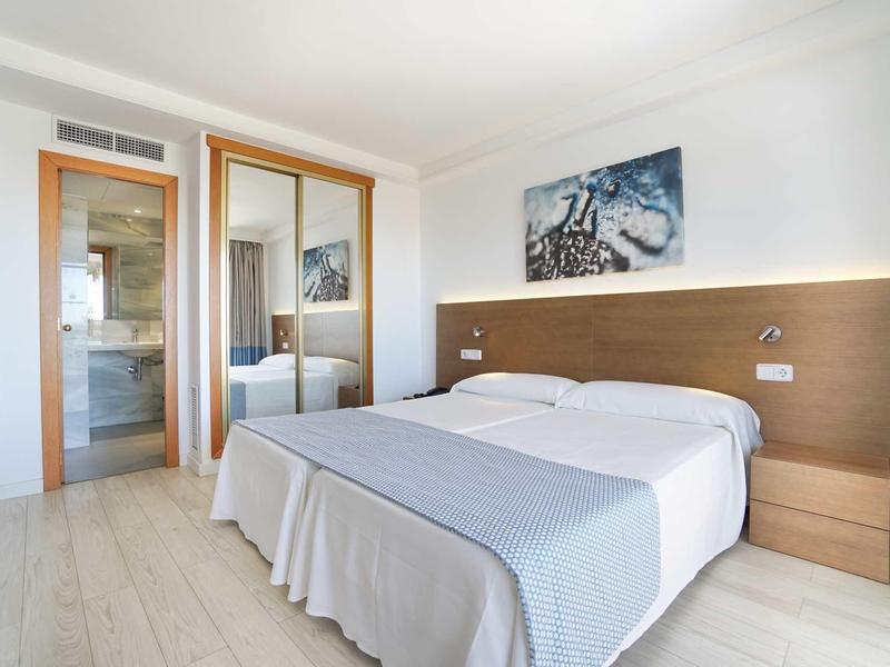 Camera d'hotel luminosa con letto matrimoniale, mobili in legno e porta del bagno moderna.