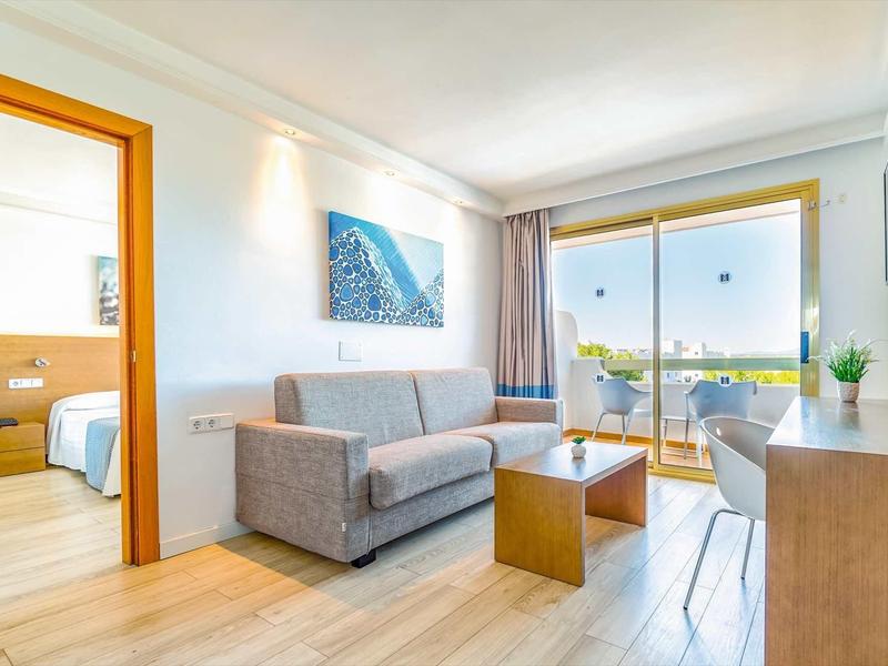 Soggiorno luminoso con divano grigio, tavolo in legno e accesso al balcone con vista.