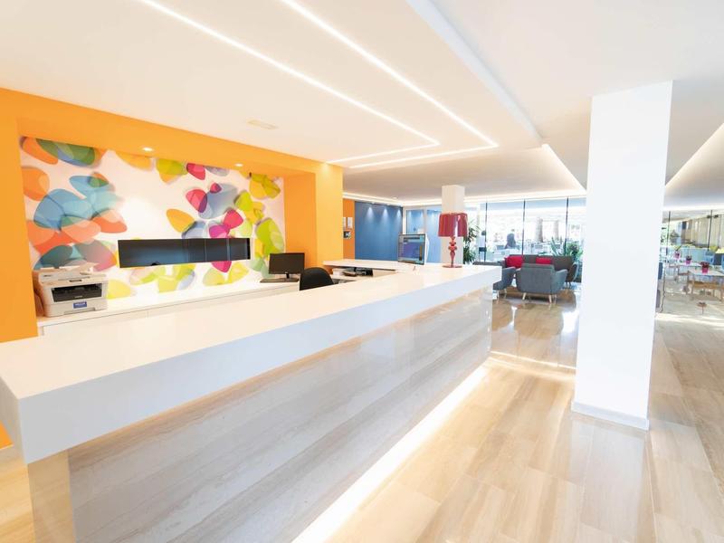 Area reception luminosa con arte murale colorata moderna e lungo bancone bianco.