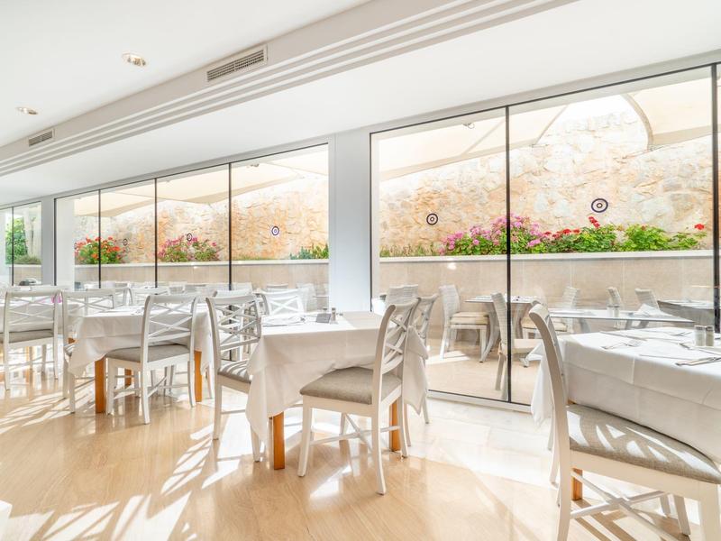 Ristorante luminoso con tavoli e sedie bianche e grandi finestre con vista sul giardino