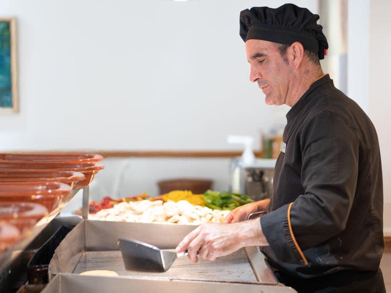 Cuoco in uniforme nero prepara cibo in una cucina a buffet.