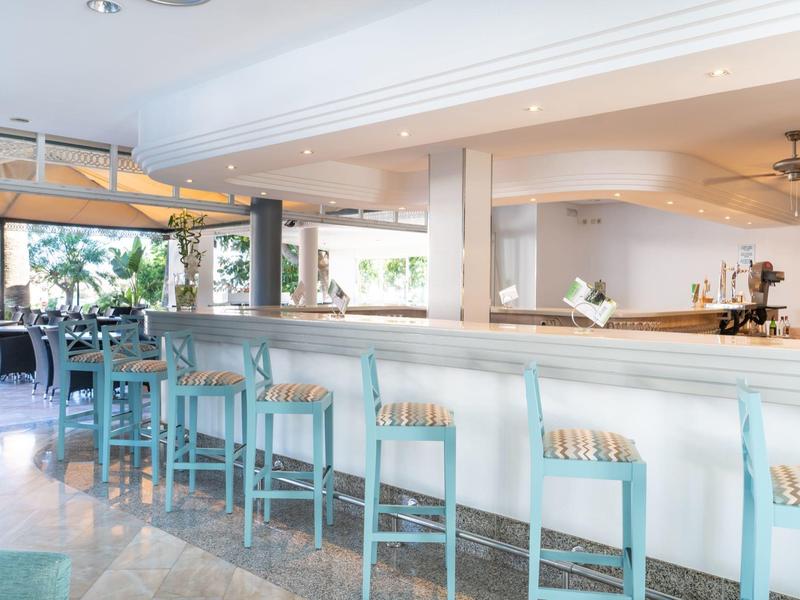 Area bar luminosa in hotel con sgabelli turchesi e finestre aperte con vista sul giardino.