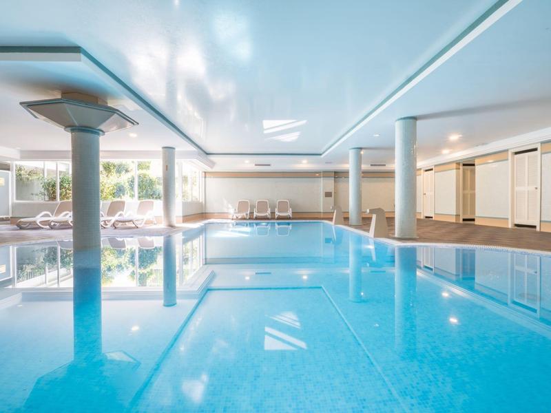 Ampia sala interna luminosa con grande piscina e sdraio per gli ospiti dell'hotel.