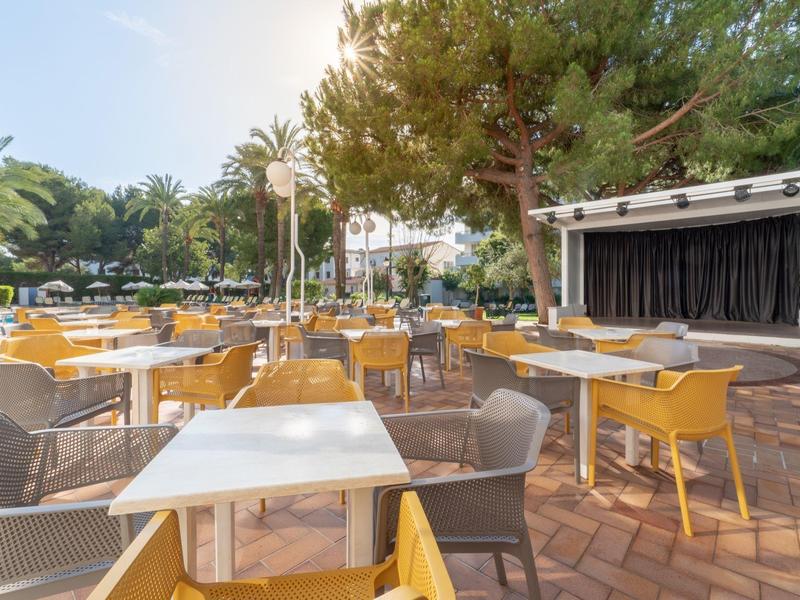 Ristorante all'aperto con tavoli e sedie sotto alberi e ombrelloni con bel tempo.