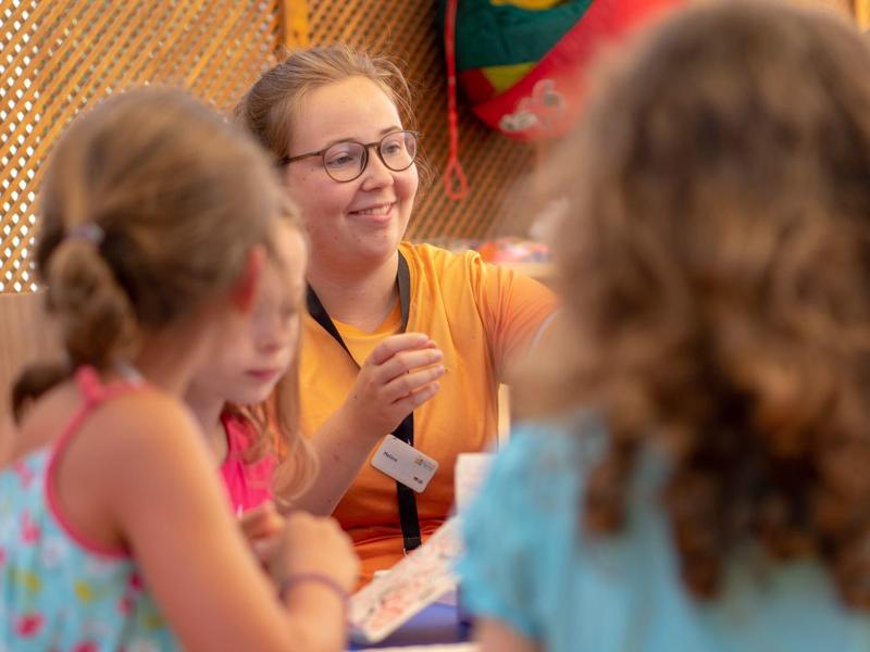 Animatrice che parla con tre bambini in un ambiente luminoso e accogliente.