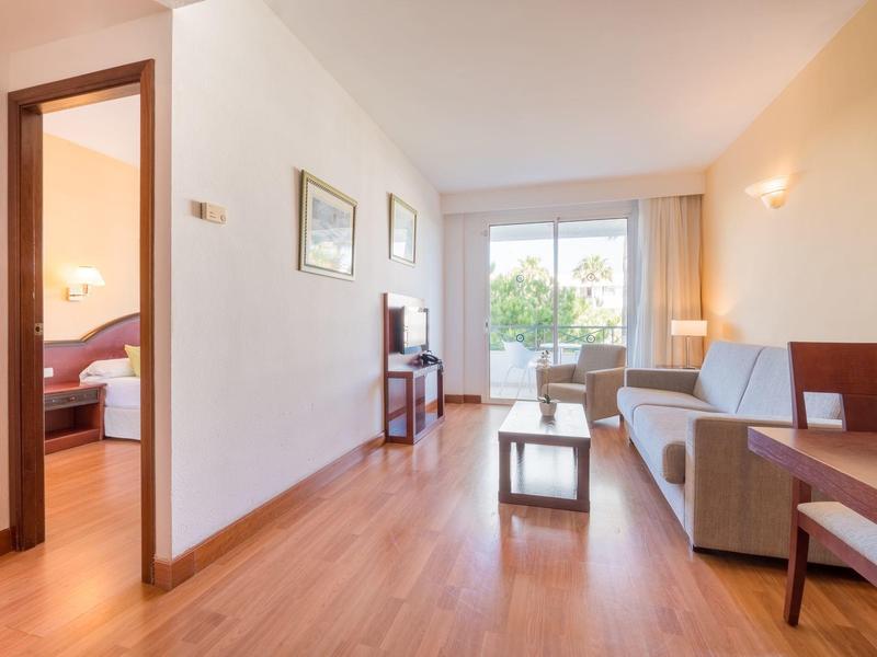 Soggiorno luminoso con divano, tavolo e accesso al balcone vicino a una camera da letto.