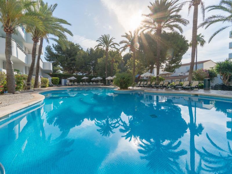 Grande piscina all'aperto con palme e lettini in una zona hotel soleggiata.