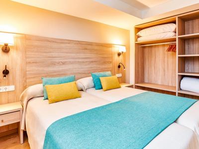 Gemütliches Schlafzimmer mit Doppelbett, türkisfarbenen Akzenten und offenem Holzkleiderschrank.