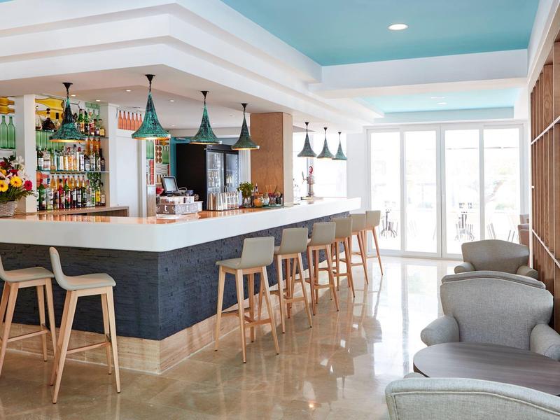 Heller Barbereich mit Holzstühlen, blauen Wänden, großer Theke und gemütlichen Sesseln am Fenster.