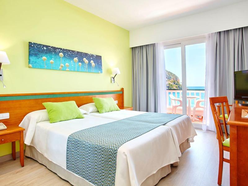 Modernes Hotelzimmer mit zwei Betten, grün-gelber Wand, Balkon und Blick aufs Meer.