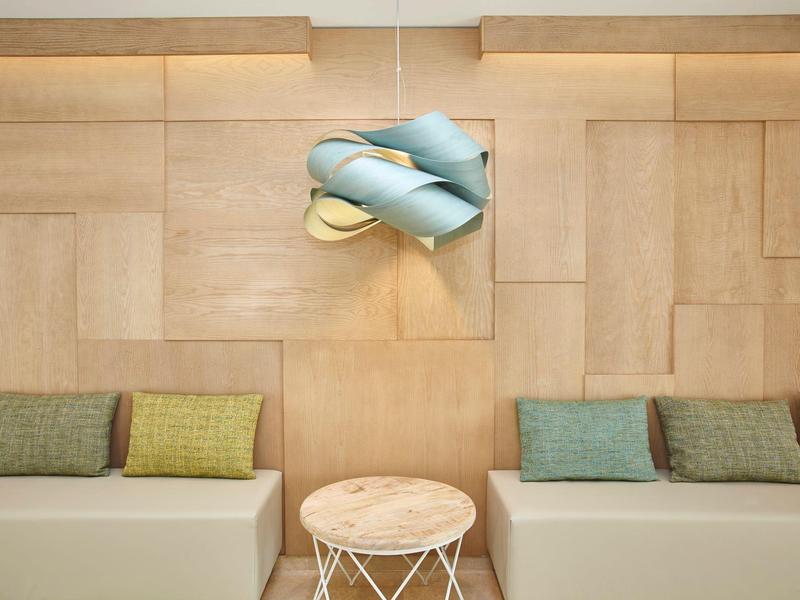 Moderner Wartebereich mit hellen Holzwänden, zwei Sofas, bunten Kissen und runder Holzablage.