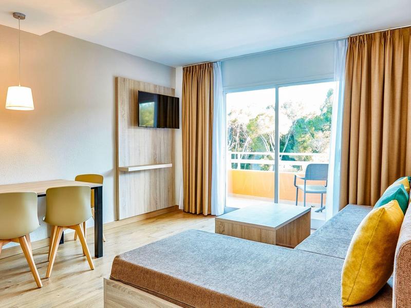 Moderner Wohnraum mit grauer Couch, bunten Kissen, Holztisch und großem Fenster mit Balkonblick.