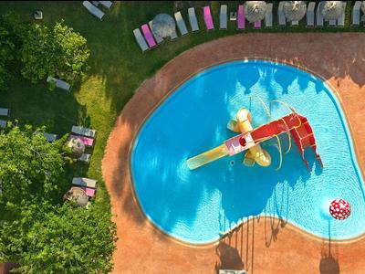 Widok z lotu ptaka na basen z zjeżdżalniami wodnymi i leżakami, otoczony drzewami.