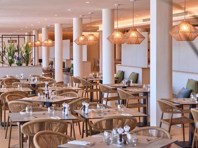 Jasna, nowoczesna restauracja z drewnianymi meblami, okrągłymi stolikami i dekoracyjnymi lampami.