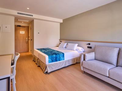 Nowoczesny pokój hotelowy z łóżkiem podwójnym, sofą i biurkiem w ciepłych kolorach.