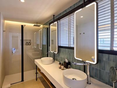 Nowoczesna łazienka hotelowa z dwoma oświetlonymi lustrami, umywalkami i dużymi oknami.