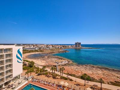 Uitzicht op een hotel met zwembad en rotskust aan de zee onder een heldere blauwe hemel.