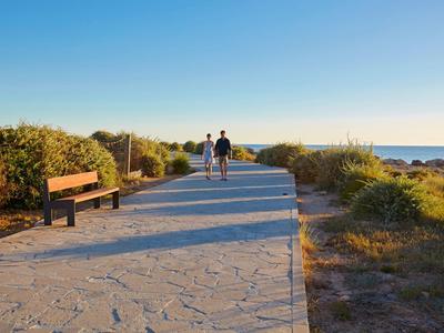 Ścieżka nad morzem z ławką i dwoma spacerowiczami przy czystym niebie