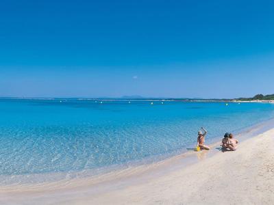Biała piaszczysta plaża z krystalicznie czystą, niebieską wodą i ludźmi odpoczywającymi na słońcu.