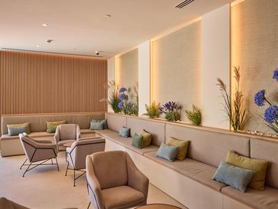 Nowoczesny, jasny salon hotelowy z wygodnymi fotelami i dekoracyjnymi roślinami przy ścianie.