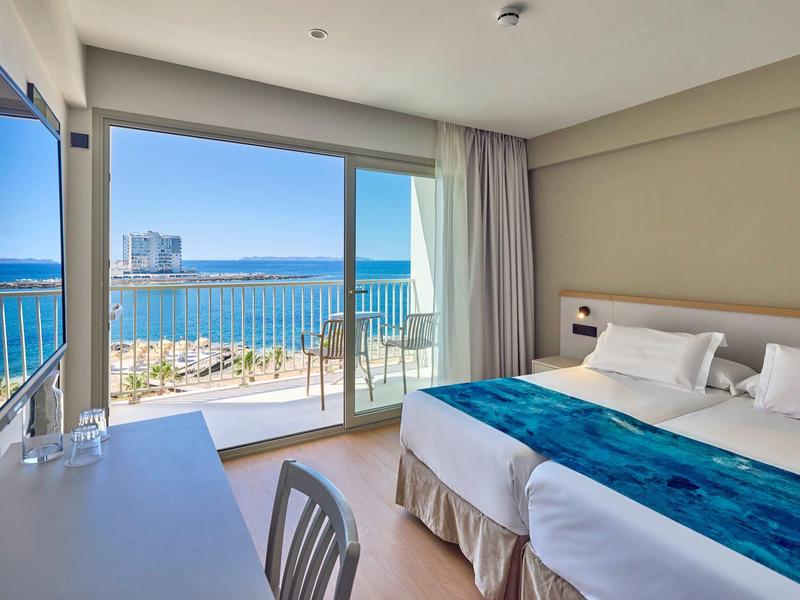 Nowoczesny pokój hotelowy z łóżkiem podwójnym i widokiem na morze przez duże szklane okno.