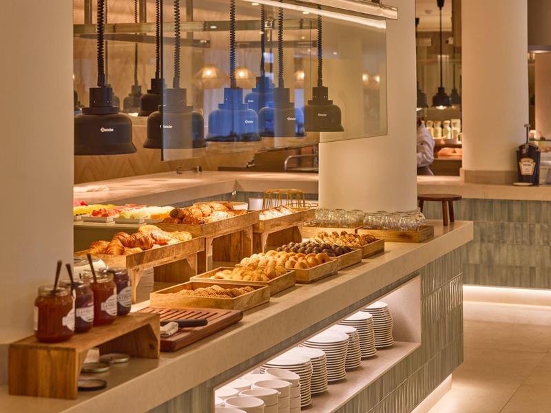 Bufet hotelowy z wyborem wypieków, dżemów i gorących dań w nowoczesnym otoczeniu.